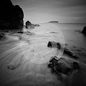 Sea waves lash line impact rock on the beach. Black and white photography.