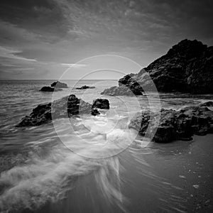 Sea waves lash line impact rock on the beach. Black and white photography.