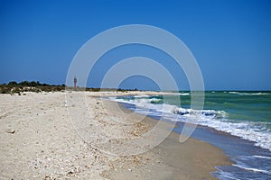 Sea waves lick the sandy coast. To the left is a lighthouse in the distance