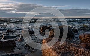 Sea waves roll on granite stones under the evening sky.