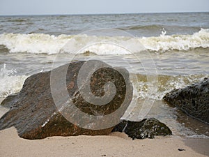 Sea waves rolling and crashing on rocks and a sandy beach on a sunny day