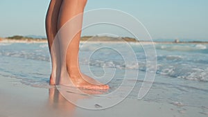 Sea waves rushing to woman legs at beach. Unknown girl standing at seashore.