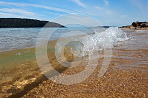 Sea waves splash on the beach with a cloudy blue sky in the background, Ettalong Beach, Australia