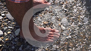 A sea waves on a stone beach covering the rocks and male feet. Media. Close up of man standing on the sea shore, summer