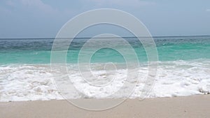Sea waves turquoise water on sandy beach on blue skyline landscape. Ocean waves splashing on sandy beach on horizon
