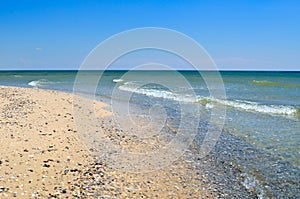 Sea waves wash the beach against a blue sky. Landscape on a wild beach. The sea in the summer