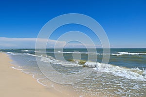 Sea waves wash the beach against a blue sky. Landscape on a wild beach. The sea in the summer