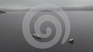 Sea yacht standing on anchor in fog on mountain landscape drone view