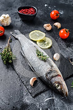 Seabass fish with herbs and lemon, raw sea bass. Black background. Top view