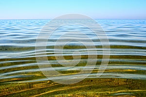 Seabed is seen through a clean and clear water. Small waves on the sea surface in summer