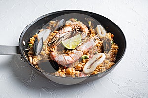 Seafood and chicken paella with rice, mussles, shrimps,chicken, tomatoes and wine in pan on white textured background