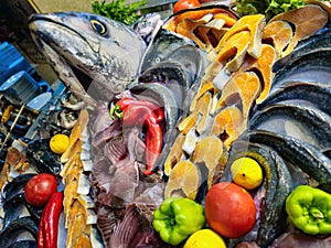 Seafood decoration with raw salmon, tuna, sea bream and other fish arranged with vegetables on ice in display of the restaurant