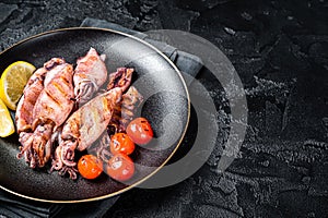 Seafood diner with grilled squid, calamary in a plate. Black background. Top view. Copy space