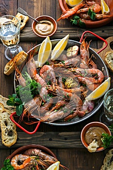 Seafood dinner. Grilled tiger prawns in grilling pan with fresh lemon, garlic, bread over wooden background, top view.