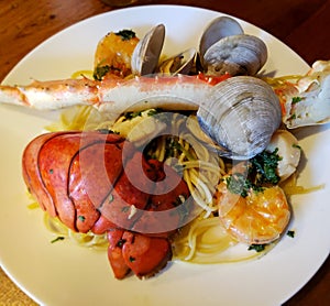 Seafood dinner plate of spaghetti, lobster tail, clams, shrimp, scallops, and crab leg