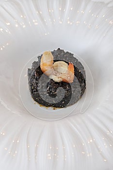 Seafood dish with black squid ink rice and a succulent shrimp perched atop, gourmet experience created with the finest ingredients