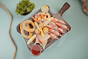 Seafood dishes with fried squid rings, shrimp and onion rings, garnished with lemon on a cutting board on a wooden