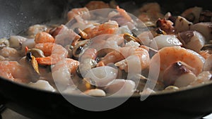 Seafood is fried in a pan. A variety of mussels, shrimps, octopuses are slow-fried in a close-up view