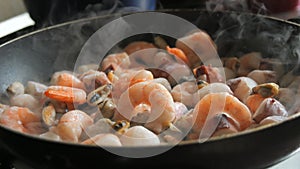 Seafood is fried in a pan. A variety of mussels, shrimps, octopuses are slow-fried in a close-up view