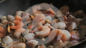 Seafood is fried in a pan. A variety of mussels, shrimps, octopuses are slow-fried in a close-up view
