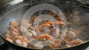 Seafood is fried in a pan. A variety of mussels, shrimps, octopuses are slow-fried in a close-up view