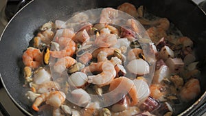 Seafood is fried in a pan. A variety of mussels, shrimps, octopuses are slow-fried in a close-up view