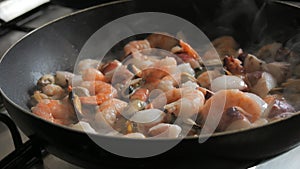 Seafood is fried in a pan. A variety of mussels, shrimps, octopuses are slow-fried in a close-up view