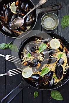 Seafood pasta. Delicious spaghetti with mussels, basil, lemon and white wine in cast iron pans on black background