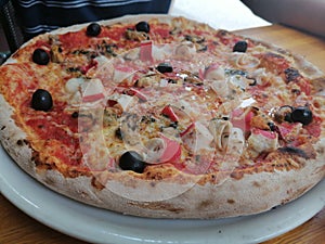 Seafood pizza with black olives on a plate in restaurant