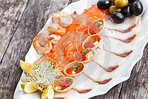 Seafood platter with salmon slice, pangasius fish, red caviar, shrimp, decorated with olives and lemon on wooden background close