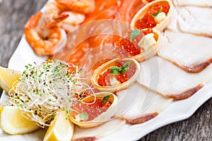 Seafood platter with salmon slice, pangasius fish, red caviar, shrimp, decorated with olives and lemon on wooden background