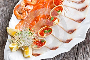 Seafood platter with salmon slice, pangasius fish, red caviar, shrimp, decorated with olives and lemon on wooden background