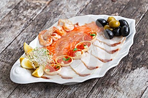 Seafood platter with salmon slice, pangasius fish, red caviar, shrimp, decorated with olives and lemon on wooden background