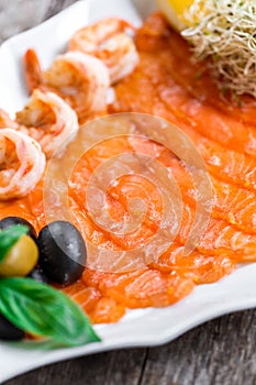 Seafood platter with salmon slice and shrimp, decorated with olives and lemon on wooden background close up