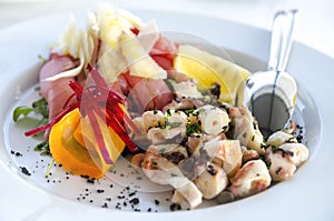 Seafood salad served in white plate closeup. Octopus and tuna fish with lemon salad appetizer on restaurant table