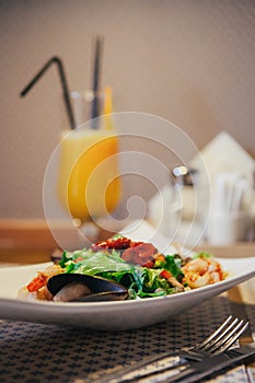 Seafood salad on the table in the cafe. Orange freshly squeezed juice on the background. indoor. Knife and fork near the