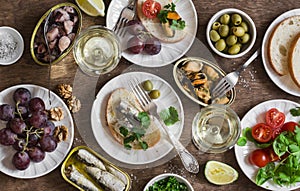 Seafood snacks table - canned sardines, mussels, octopus, grape, olives, tomato and two glasses white wine on wooden table, top vi
