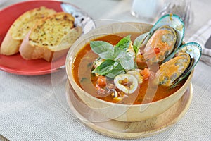 Seafood tomato soup served with garlic bread on cutting board an