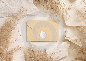 Sealed envelope near beige travertine stones and dried pampas grass top view, greeting mockup