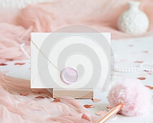 Sealed envelope near pink decorations, hearts and tulle on white table close up, mockup