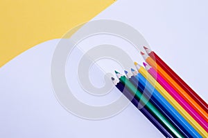 Seamless colored rainbow pencils on sheets of white paper school drawing album on yellow background isolated. Concept of free