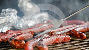 Seamless loop - Fork turning over tasty juicy sausages grilling on a barbecue with potatoes in foil, video HD