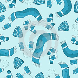 Seamless pattern with winter clothes, scarfs, hats, gloves and mittens and socks wirt snowflakes on a blue background.