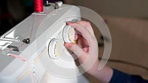 The seamstress chooses the mode on the sewing machine. She rotates the switch with her hand. The camera slides to the