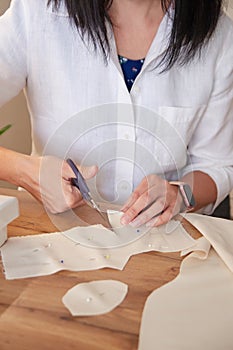 Seamstress cutting beige fabric with scissors