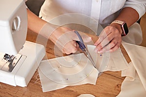 Seamstress cutting beige fabric with scissors