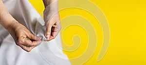Seamstress hands with white cloth on bright trendy color yellow background. Female hands with a needle, thread and thimble. Women