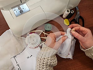 Seamstress holds fabric together with ball-point pins. Female hands pin a pattern of a medical face mask on the background of