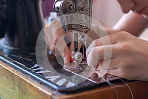 A seamstress inserts a thread into a needle eye on an old retro sewing machine.