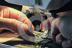 Seamstress inserts the thread through the needle threader of the sewing machine